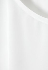 Top blanco sin mangas hecho de una tela suave con escote redondo. La textura es ligera y ligeramente elástica. Diseño simple.
