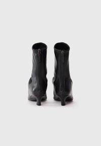Bottines en cuir noir avec un talon fin, dotées d'une fermeture éclair au dos et d'une texture lisse. Le design est ajusté au niveau de la cheville.