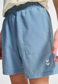 Ljusblå shorts i mjukt tyg, med elastisk midja, två sidofickor och en vit zigzag-mönstring på underbenet.