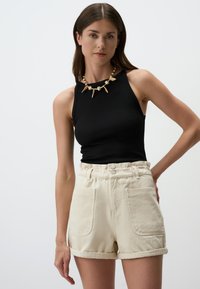 Top nero a costine senza maniche abbinato a pantaloni corti alti di colore crema con orli arrotolati e tasche frontali.