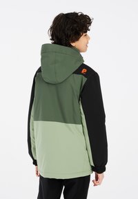 Hoodie in Dunkelgrün, Schwarz und Hellgrün. Ausgestattet mit elastischen Bündchen, einer glatten Außenseite und einem orangenen Logo auf der Schulter.