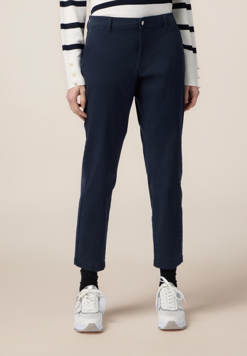 Marinblå, slim-fit byxor i ett mjukt tyg, med knappstängning och sidofickor, ihop med vita sneakers och svarta strumpor.