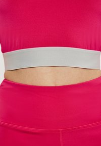 Rózsaszín sport crop top fehér rugalmas pánttal az alján. Sima, rugalmas textúra. Magas derekú alsókkal viselve.