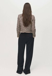 Giacca marrone con texture, dal design cropped, abbinata a pantaloni neri larghi. Finitura evidente all'orlo della giacca.