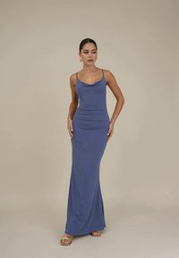 Vestido longo e justo em tecido azul suave, com alças finas, decote redondo e uma silhueta solta que se estende até ao chão.