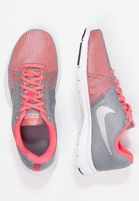 Šedé sportovní boty s růžovými akcenty, síťovaný svršek, zaoblená špička, bílý Nike swoosh, lehký design a texturovaná gumová podrážka.