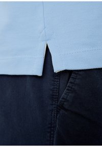 Svetle modré polo triko s texturovaným pletením, s bočním rozparkem a kontrastním krémovým lemováním, kombinované s tmavě námořnickými kalhotami.