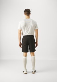 Svarta sportshorts med elastiskt midjeband, i kombination med en åtsittande vit t-shirt och knähöga vita strumpor, sett bakifrån.