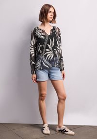 Blusa trasparente a righe bianche e nere con maniche lunghe, abbinata a pantaloncini di denim blu chiaro e sneakers beige con dettagli neri.