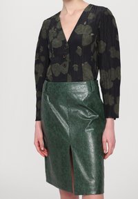 Černá halenka se zeleným květinovým potiskem a třemi knoflíky, spojená se zelenou sukní tužkového střihu z umělé kůže s předním rozparkem.