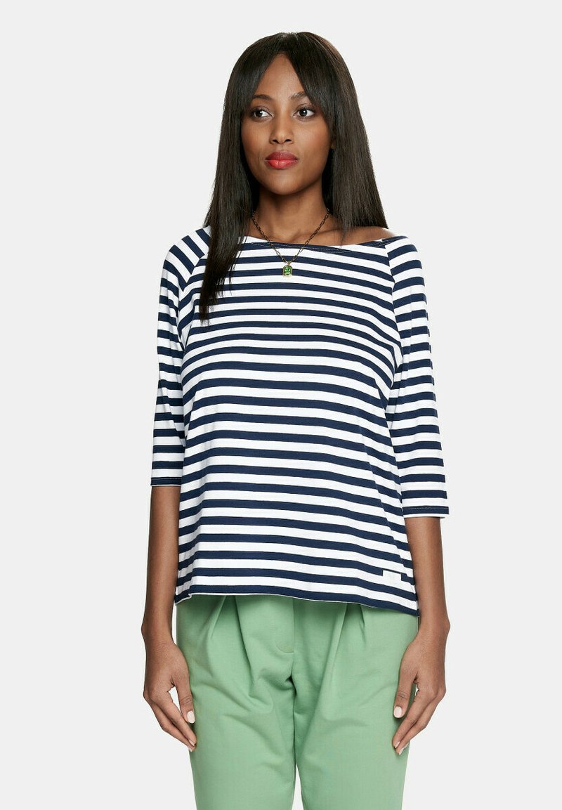 Koszula w pasy w kolorze granatowym i białym, z rękawami trzyczwartowymi, luźny krój i szeroki dekolt. Noszona z zielonymi spódnicą plisowaną.