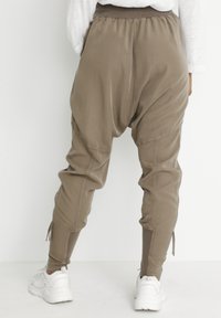 Khaki harembyxor med elastisk midja, åtsittande manschetter och sidor. Tillverkade av ett mjukt, lätt tyg. Stylet med vita sneakers.