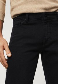 Jean en denim noir avec une coupe slim, doté d'un design à cinq poches et de coutures avant discrètes. Le matériau semble lisse et durable.