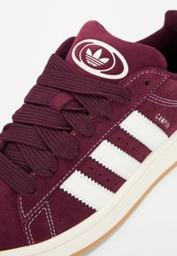 Burgunderfarbene Wildledersneaker mit weißen Lederstreifen, strukturierten Schnürsenkeln und einem Logo-Patch auf der Zunge. Gummigummi-Außensohle.