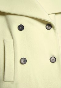 Dvojité sako v jemně žluté barvě, vyroben�é z měkké látky. Obsahuje tmavé knoflíky a klopový límec, s boční kapsou.