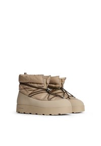 Beige isolierte Knöchelstiefel mit einem dicken Nylon-Obermaterial, geschnürt mit braunen Schnürsenkeln, und einer dicken, strukturierten Gummisohle für guten Halt.