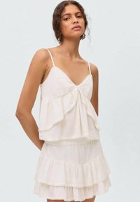 White, layered dress with thin straps, featuring ruffles and lace trim. Made of lightweight fabric, with a loose fit and a flowing design.