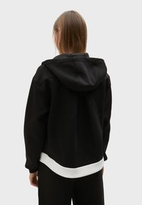 Crna dukserica s kengurudžepom, poznata po mekom materijalu i opuštenom kroju. Sadrži bijeli rub kao akcent i prostranu kapuljaču.