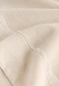 Țesătură texturată de bej deschis, cu nervuri fine, care prezintă fibre moi și cusături vizibile. Materialul pare confortabil și cald.