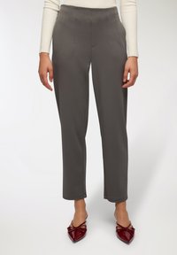 Szare spodnie o prostym kroju, z zaszewkami z przodu i gładką fakturą, w połączeniu z bordowymi płaskimi butami na spiczastym nosku.