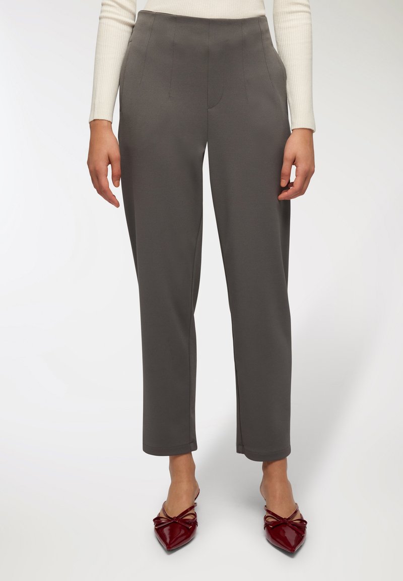 Szare spodnie o prostym kroju, z zaszewkami z przodu i gładką fakturą, w połączeniu z bordowymi płaskimi butami na spiczastym nosku.