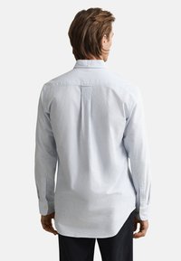 Šviesiai mėlyna ir balta dryžuota marškinėliai su apykakle, išlenktu apvadu ir sagomis užsegamais rankogaliais, pagaminti iš lygios medžiagos.