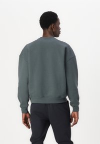 Mörkgrön sweatshirt med rund halsringning, sänkt axelsöm och ribbad manchetter och nederkant. Har ett mjukt, texturerat tyg.