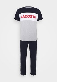 Súprava na voľný čas v sivej a námorníckej modrej farbe pozostávajúca z dvoch kusov. Tričko s červeným logom "LACOSTE", vyrobené z bavlny, s voľnejším strihom. Nohavice sú námorníckej modrej farby s rovnom strihom.