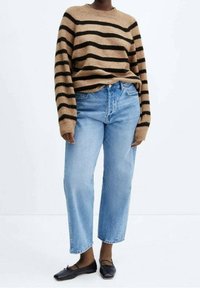 Pull en rayures marron et noir avec des manches longues, associé à un jean en denim taille haute bleu clair et des ballerines noires. Textures lisses.