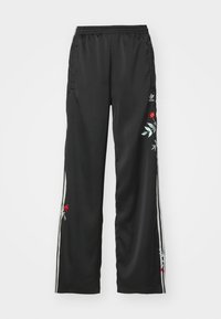 Svart sportbyxor med vita sidostrek, prydda med röd och grön blommönstring på vänster ben. Tillverkade av ett mjukt och lätt material.