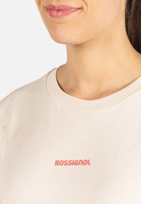 Béžové bavlněné tričko s kulatým výstřihem a krátkými rukávy. Na přední straně se nachází výrazné červené logo "ROSSIGNOL".