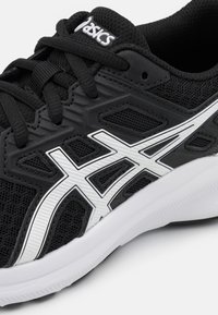 Chaussure de sport noire en matériau en maille, avec des lignes d'accent blanc et une semelle texturée. Comprend des œillets renforcés et un logo sur la languette.