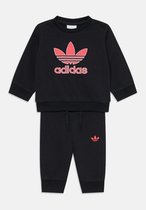 Fekete sportöltöny hosszú ujjakkal és nadrággal. A mellkason egy rózsaszín Adidas logó található, valamint egy kisebb logó a bal nadrágon.