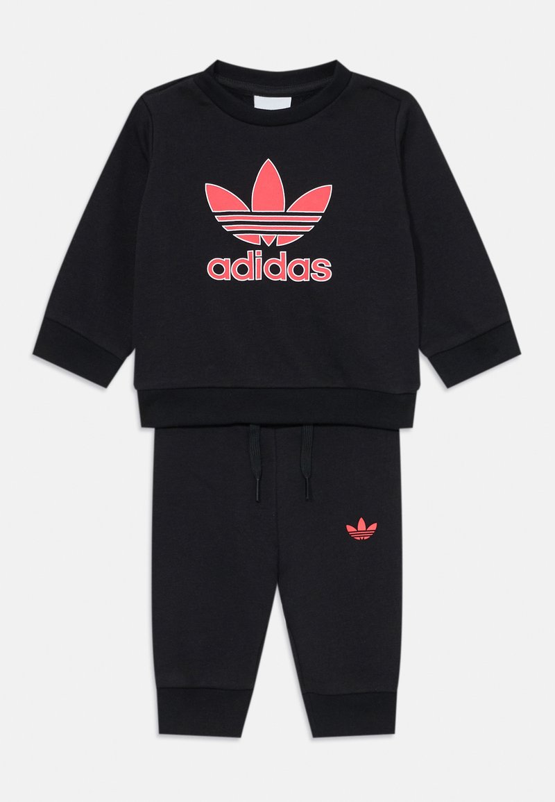 Melnas sporta tērps ar garām piedurknēm un biksēm. Ar rozā Adidas logotipu uz krūškurvja un mazāku logotipu uz kreisās bikses kājas.