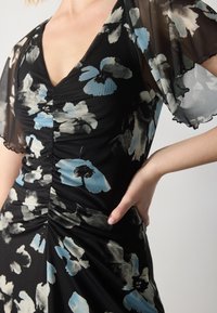 Black floral dress featuring a fitted bodice with ruching, sheer flutter sleeves, and a V-neck. Flowers in shades of blue and gray.