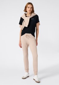 Zwart T-shirt met een logo, beige sweatpants met een trekkoord en witte sneakers met grijze accenten. Casual outfit voor ontspannen draag.