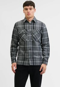 Camisa de cuadros gris hecha de franela, con dos bolsillos en el pecho, cierre de botones y cuello. Tejido texturizado con patrones de cuadros distintivos.