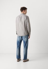 Grijze longsleeve shirt met een rechte snit, knoopmanchetten en een rugplooi, gecombineerd met lichtblauwe denim jeans en browne schoenen.