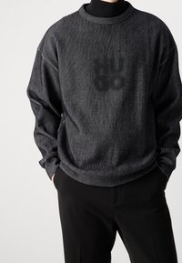 Pull rayé noir avec col rond et coupe ample. Tissu texturé et imprimé discret à l'avant. Associé à un pantalon noir.