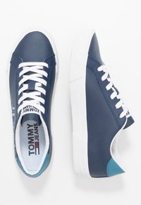 Navy blue leather sneakers with white laces and rubber soles. Features a logo detail and a contrasting light blue accent on the heel.