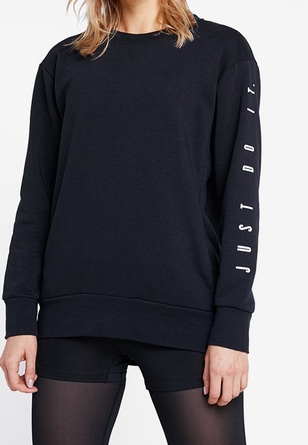 Personne portant un sweat-shirt noir à manches longues avec « JUST DO IT. » imprimé verticalement sur la manche droite et un short noir.