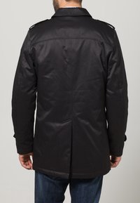 Svart, lång kappa med en slät yta och två bakvickar. Har axelremmar på axlarna och en skräddarsydd passform.