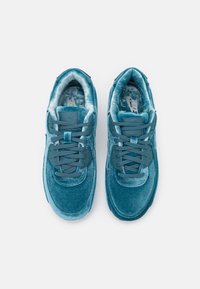 Sammetsgröna sneakers med vadderad krage, snörningsdesign, texturerad yta och framträdande varumärke på innersulan och tungan.