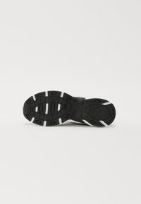 Black athletic shoe sole featuring multi-directional tread pattern, textured rubber, and white accents. Curved edges at the heel.
