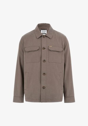 Barna pamut dzseki hegyes gallérral, gombos záródással, két mellzsebbel és finom logó részlettel. Sima textúra, egyenes szabás.