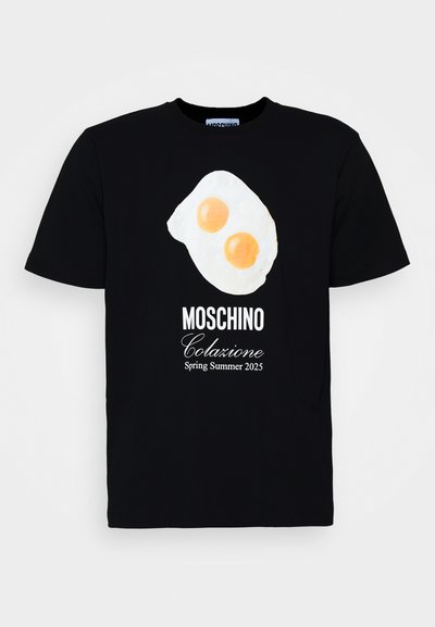 Black cotton t-shirt featuring a graphic of fried eggs with two orange yolks. "Moschino Colazione Spring Summer 2025" printed in white.
