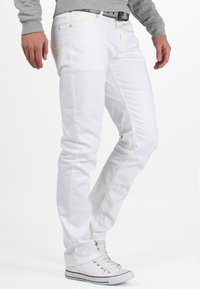 Jeans en denim blanc avec des coutures jaunes, coupe slim et design à jambe droite. Associés à des baskets blanches pour un look décontracté.