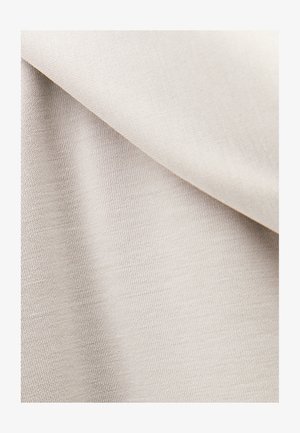 Tissu tissé beige clair plié en diagonale, montrant une texture lisse et un motif de tricot fin sous un éclairage doux.