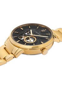 Reloj de tono dorado con un dial negro, con mecanismos expuestos, tres subdiales y una pulsera de metal con acabado pulido.