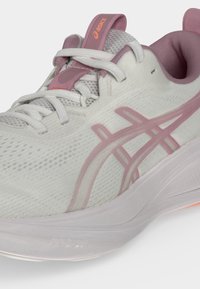 Λευκό και ροζ αθλητικό παπούτσι τρεξίματος Asics με διχτυωτό πάνω μέρος, λευκά κορδόνια και μαλακή σόλα, εμφανίζεται από κοντινή πλαϊνή γωνία.